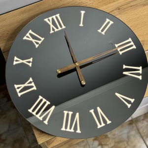 May include: A black round clock with Roman numeral markings in white. The clock hands are gold and brown.