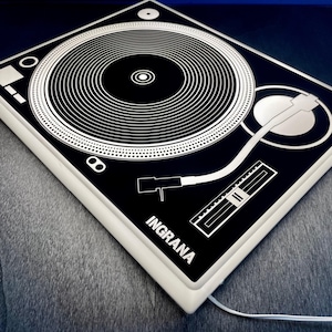 May include: A black and white turntable design with the word "INGRANA" printed on the front. The turntable features a circular record, tone arm, and control panel. The design is set in a white square frame.
