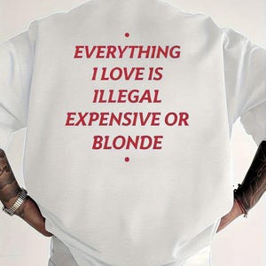 May include: A white sweatshirt with the phrase "EVERYTHING I LOVE IS ILLEGAL EXPENSIVE OR BLONDE" printed in red. The sweatshirt is a casual style, with a crew neck and long sleeves. The image shows the back of the sweatshirt.