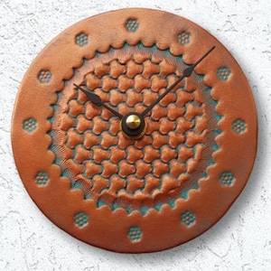 May include: A round, brown leather wall clock with a decorative, teal and copper design. The clock has black hands and a gold center.