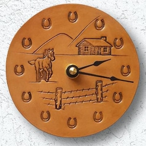 May include: A brown leather clock with a horse, a small house, and a fence design. The clock face is surrounded by horseshoes.