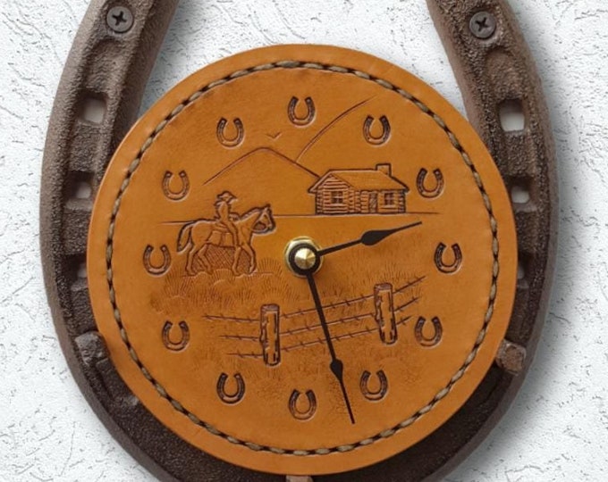 Leather horseshoe clock with a ranch scene of cowboy or cowgirl on a horse, log cabin, and barbed wire fence, all hand-tooled into leather.
