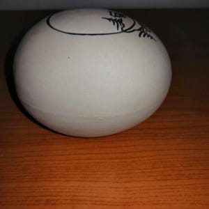 Pode incluir: Um pote redondo de cerâmica branca com um desenho de árvore preto no topo.