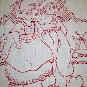 Op de afbeelding: Rood geborduurde afbeelding van twee kinderen in traditionele kleding, op een witte linnen achtergrond.
