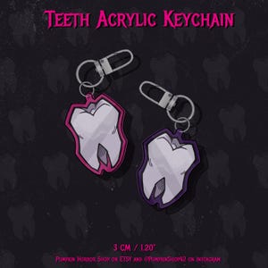 Könnte beinhalten: Zwei Acryl-Schlüsselanhänger mit einem Zahndesign, umrandet in Pink und Lila. Sie haben silberne Verschlüsse und sind 3 cm groß. Der Text "TEETH ACRYLIC KEYCHAIN" steht oben.