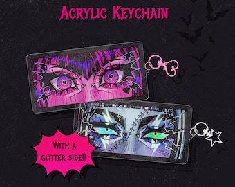 May include: Two acrylic Monster High keychains featuring stylized eye designs. One keychain has pink and purple eyes, the other has blue and green eyes. The keychains are 2.75 inches long and have a glitter side. The text "Monster High Acrylic Keychain" is at the top.