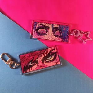 Può includere: Due portachiavi in acrilico con illustrazioni ravvicinate di occhi con accenti rosa e viola. Gli occhi sono spalancati e hanno un'espressione drammatica. Un portachiavi ha un ciondolo a forma di stella.