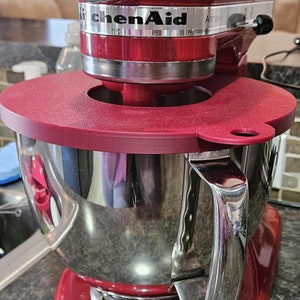 May include: A red KitchenAid Artisan stand mixer with a silver bowl and a red silicone splash guard. The mixer has a silver knob and a silver lever on the side.