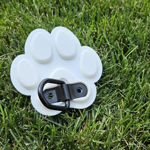 May include: White plastic paw print with a black metal D-ring attached. The paw print has five raised bumps.