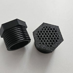 May include: Two black plastic fittings on a white surface. One fitting has external threads and a hexagonal head. The other fitting is hexagonal with a perforated surface. Both are likely used for plumbing or industrial applications.