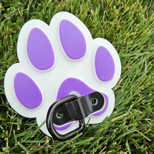 May include: White plastic dog paw print with purple accents and a black metal D-ring.