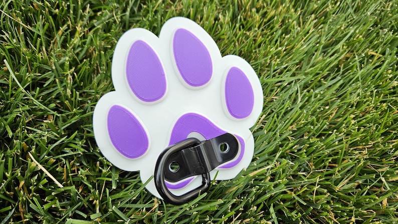 May include: White plastic dog paw print with purple accents and a black metal D-ring.