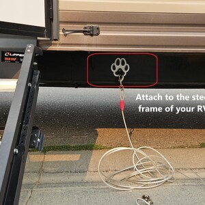 May include: A silver paw-shaped hook attached to the steel frame of a recreational vehicle (RV). A silver cable is connected to the hook.