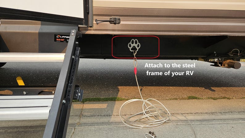 May include: A silver paw-shaped hook attached to the steel frame of a recreational vehicle (RV). A silver cable is connected to the hook.