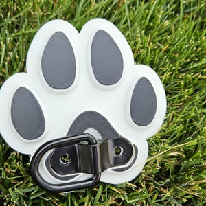 May include: White plastic paw print with black paw pads and a black metal D-ring.