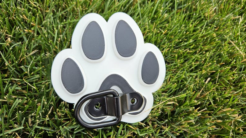 May include: White plastic paw print with black paw pads and a black metal D-ring.