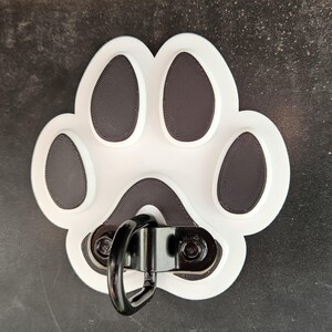 May include: White plastic paw print with a black metal ring attached. The paw print has four black toes and a black outline.