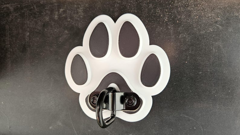 May include: White plastic paw print with a black metal ring attached. The paw print has four black toes and a black outline.