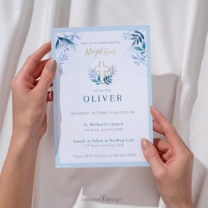 Puede incluir: Una invitación de bautizo azul claro con detalles florales y una cruz dorada. La invitación dice "Únase a nosotros para celebrar el bautizo de nuestro hijo Oliver" e incluye detalles del evento. El diseño presenta una corona floral y el texto "bloszom design".