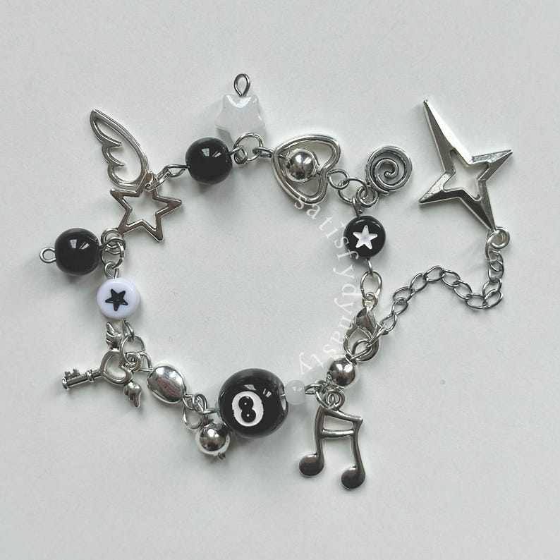 May include: A silver charm bracelet with black and white beads, charms include a star, a heart, a key, a music note, a wing, and a black 8-ball.