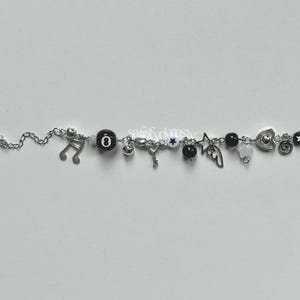 May include: A silver charm bracelet with black and white beads and charms, including a star, music note, key, heart, and wings.