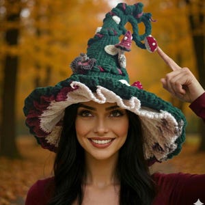 May include: A whimsical, handmade crochet witch hat in shades of green, white, and burgundy. The hat features a wide brim with a ruffled edge and is adorned with mushroom and floral accents. The hat is a unique accessory for costume or cosplay.