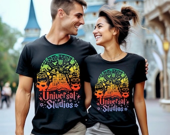 May include: Black t-shirts with a vibrant graphic design featuring cartoon characters, a castle, and the text "Universal Studios." The design includes a rainbow gradient and stars. The shirts are worn by a couple.