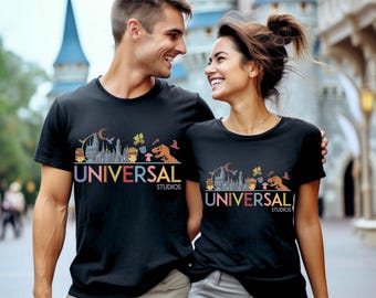 May include: Black t-shirts with a colourful graphic design and the text "UNIVERSAL STUDIOS". The design includes cartoon characters, a castle, and a crescent moon. The shirts are worn by a couple.