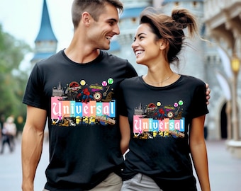 May include: Black t-shirts with a colourful graphic design featuring the word "Universal" and various theme park icons. The design includes images of a castle, dinosaurs, Spider-Man, and the Minions.