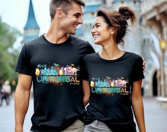 May include: Black t-shirts with a colourful graphic design featuring the text "UNIVERSAL STUDIOS". The design includes cartoon characters and a cityscape. The shirts are worn by a couple.