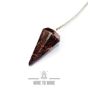 May include: A faceted, reddish-brown crystal pendulum suspended from a silver chain. The crystal has a geometric shape with multiple facets. The image includes the text "MINE TO MIND" below a graphic of a person meditating.
