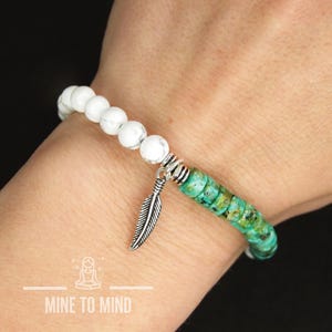 May include: White and turquoise beaded bracelet with a silver feather charm. The bracelet is made with small round beads and has a silver clasp.