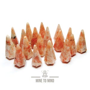 May include: A group of 17 sunstone crystal points in various shades of orange and white. The points are arranged in a semi-circle on a white background.