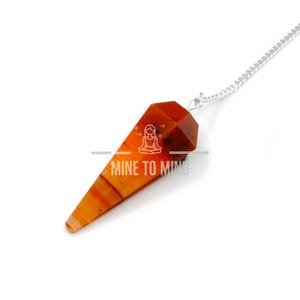 May include: A carnelian crystal pendulum with a silver chain. The pendulum is a pointed, faceted shape with orange and red hues.