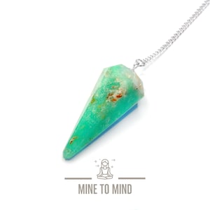 May include: A green and white crystal pendulum on a silver chain. The pendulum is shaped like a teardrop and has a pointed tip. The crystal is translucent and has a speckled pattern. The chain is attached to the top of the pendulum.