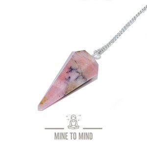 Könnte beinhalten: Ein rosa-weißes Opal-Kristallpendel mit einer silbernen Kette. Das Pendel ist tropfenförmig und hat eine spitze Spitze. Die Kette ist an der Oberseite des Pendels befestigt.