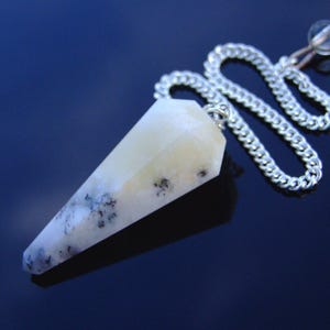 May include: White and gray crystal pendulum with a silver chain. The pendulum is pointed and has a clear crystal at the end of the chain.
