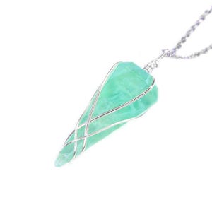May include: A pendant necklace with a light green, pointed crystal encased in silver-coloured wire. The crystal hangs from a delicate silver chain, creating a simple yet elegant design. The necklace is set against a white background.
