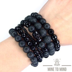 May include: Several black beaded bracelets, including lava rock and onyx beads, and a skull-shaped bead. The bracelets are stacked on a wrist. The image includes the text "MINE TO MIND".
