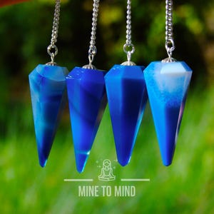 May include: Four blue agate crystal pendulums with silver chains hanging against a green background. The pendulums are all pointed at the bottom and have a white swirl pattern.