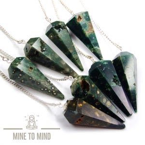 May include: A collection of six pointed, faceted green moss agate pendants, each suspended from a silver-toned metal chain. The stones feature dark green hues with natural inclusions, crystalline cavities, and light-colored spots. Logo: MINE TO MIND.