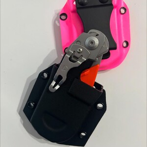 May include: A black and pink knife sheath with a silver pocket knife with an orange handle. The knife is partially inserted into the black sheath.