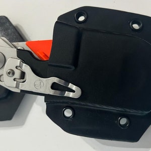May include: A black leather knife sheath with a silver clip and a small orange knife inside.