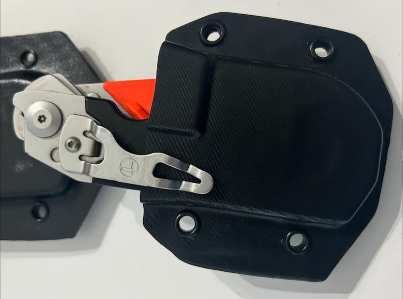 May include: A black leather knife sheath with a silver clip and a small orange knife inside.