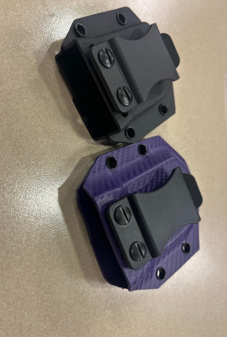 May include: Two gun holsters, one black and one purple with a carbon fiber pattern. Both holsters have a black clip.