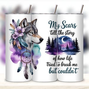 May include: White tumbler featuring a wolf with floral and feather accents, and a dreamcatcher. The tumbler has the text "My Scars tell the story of how life tried to break me but couldn't". Includes a silver straw.