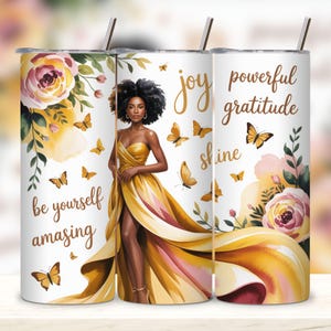 May include: A white tumbler with a design featuring a woman in a yellow gown, butterflies, and floral accents. The tumbler has the words "be yourself amazing", "joy", "shine", and "powerful gratitude". Includes a silver straw.