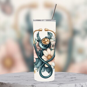 Puede incluir: Un vaso blanco con un dise&ntilde;o floral y un estetoscopio. El estetoscopio es azul verdoso con detalles dorados. Las flores son rosas, blancas y verdes.
