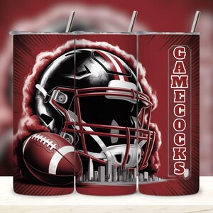 May include: A red and black tumbler featuring a football helmet and football. The helmet is black with white stripes and red accents. The word "Gamecocks" is printed vertically on the side of the tumbler.