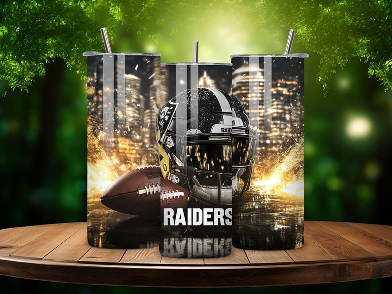 K&ouml;nnte beinhalten: Drei Edelstahlbecher mit einem schwarz-wei&szlig;en Design, das einen Footballhelm mit dem Wort "RAIDERS" zeigt. Der Hintergrund ist ein verschwommenes Bild einer Skyline.